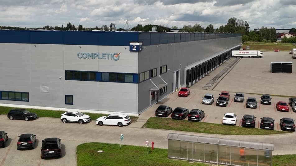 The Completio Central Warehouse in Łódź from outside: the facade with the Completio logo, loading docks with trailers, and the car park