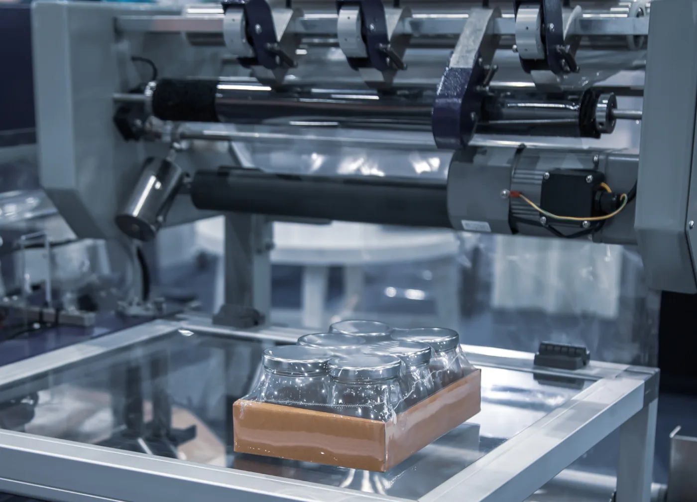 Shrink-wrap machine: a product moving along the belt under the film roll inside the chamber